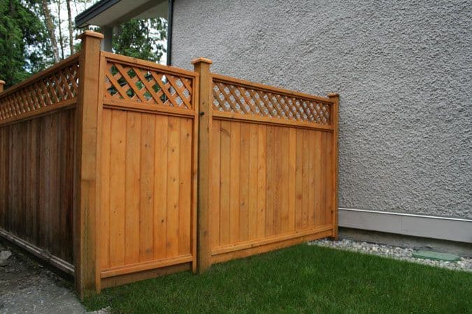 Corner of a cedar privacy fence with diagonal lattice top beside a stucco wall