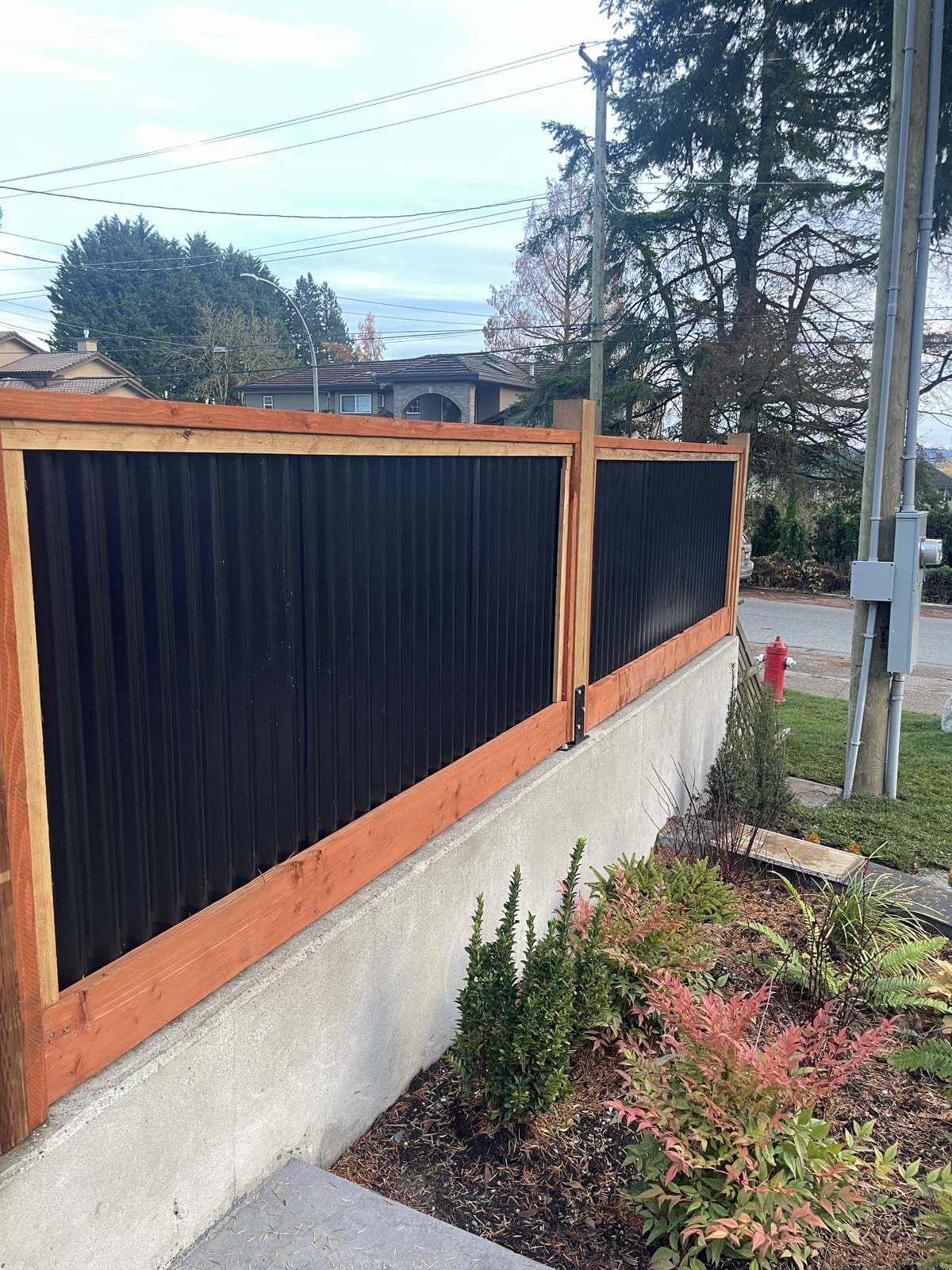 Wood and steel fence panels above a concrete wall on a landscaped corner