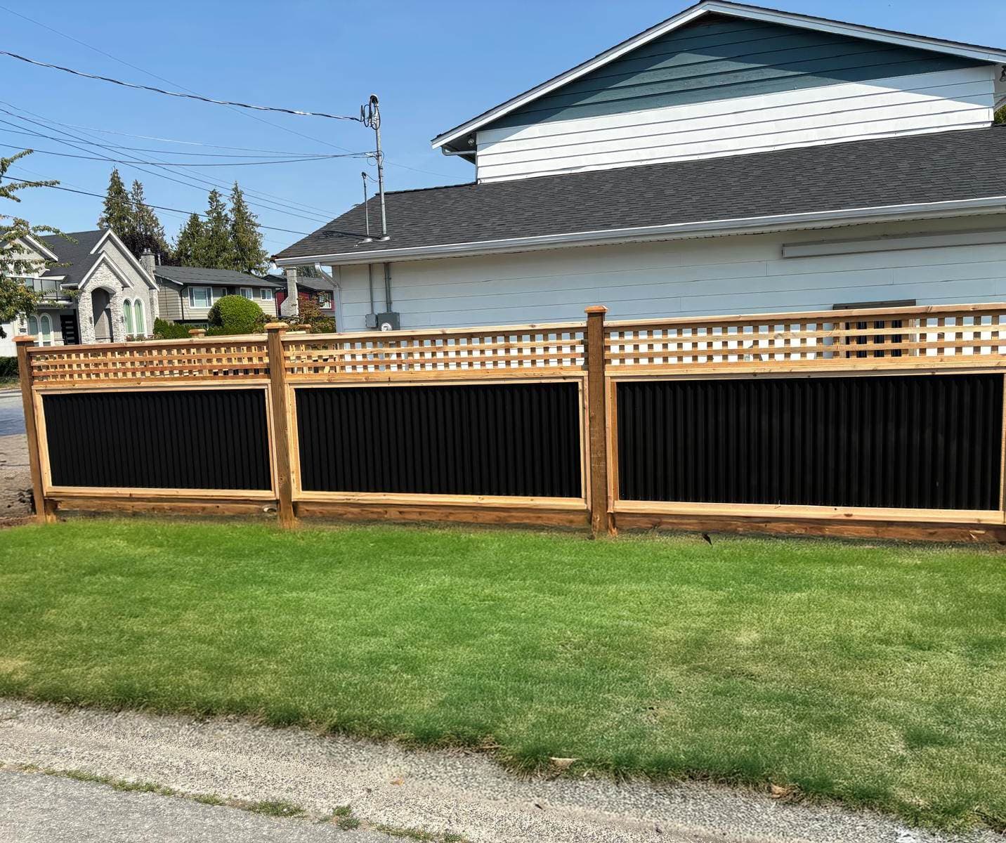 Fence of black corrugated steel panels with square lattice tops in cedar frames